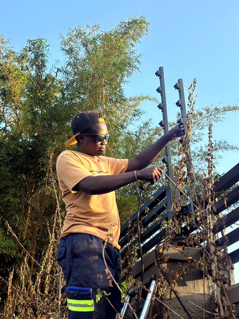 Technician fixing electric fence brackets and wires on top of a boundary wall