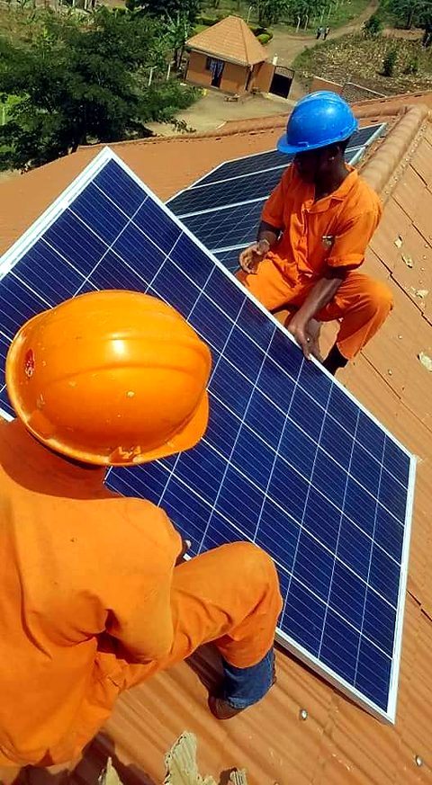 Two Trivox technicians in orange overalls and hard hats installing solar panels on a tiled roof